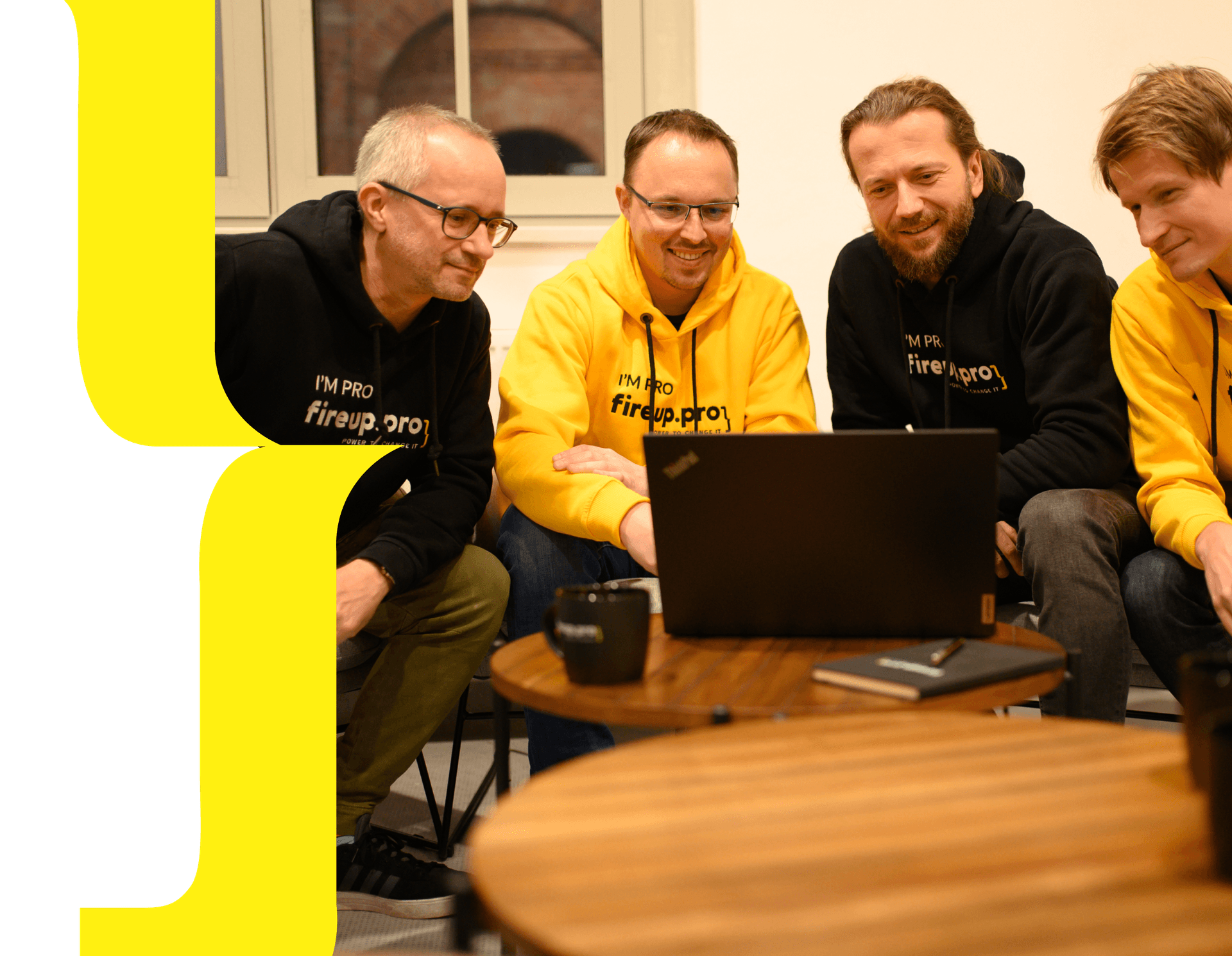 Three developers from fireup.pro are hard at work creating modern applications, dressed in company sweatshirts that feature an elegant combination of black and yellow, along with the distinctive software development company logo. The team, immersed in an atmosphere of creativity and technological innovation, collaborates on the project using advanced development tools to deliver top-quality solutions for their clients.