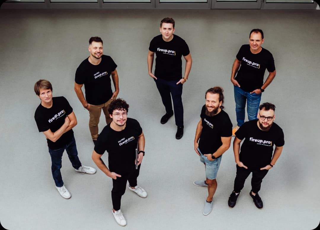 Seven smiling team members of fireup.pro, wearing company shirts with the logo, ready to take on projects for international clients. Our offerings include, among others, IT consulting services.